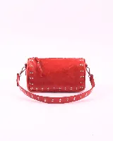 Bandolera de cuero natural color rojo, con diseño rectangular y detalles de tachas metálicas en los laterales y en la correa. Cuenta con cierre superior y dos asas desmontables.