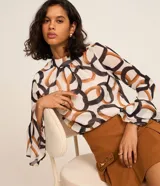 Blusa de chiffon con estampa de eslabones y argollas entrelazadas en tonos marrones y negros sobre fondo blanco. Presenta cuello alto, mangas largas acampanadas y cierre tipo gota en la espalda.