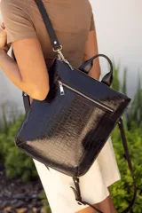 Mochila negra de cuero con textura tipo cocodrilo, doble asa corta superior y correa larga regulable para usar al hombro o como mochila. Cierre superior con cremallera y bolsillo frontal con cremallera.