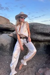 Conjunto de dos piezas confeccionado en seda plisada color beige. Incluye una blusa sin mangas con volados en los hombros y un pantalón de corte holgado con puños elásticos fruncidos en los tobillos.