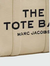 Bolso tote Marc Jacobs modelo The Jacquard, confeccionado en tejido de lona negro con detalles en blanco. Presenta el logo de la marca y la inscripción 'THE TOTE BAG' en el frente, con doble asa superior y correa ajustable extraíble.