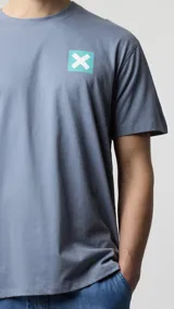 Camiseta de manga corta color verde azulado, corte holgado, con un pequeño estampado cuadrado con una 'X' en el pecho.