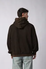 Buzo canguro de corte oversize, confeccionado en frisa de algodón con efecto de lavado gastado. Presenta un aplique decorativo cosido al corte en el centro del pecho, capucha amplia y bolsillo frontal tipo canguro.