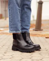 Botinetas de cuero negro con suela track dentada. Presentan una combinación de texturas en el lateral, con una sección de cuero liso y otra con textura grabada, además de un panel elástico en la parte superior del tobillo.