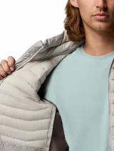 Campera puffer híbrida Columbia modelo Powder Pass Hybrid, de color gris claro con paneles laterales en tono marrón oscuro. Cuenta con cuello alto, cierre frontal completo y bolsillos laterales con cierre. Logo de la marca bordado en el pecho.