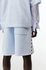 Short de felpa celeste de corte regular fit, con cintura elástica y cordón ajustable. Cuenta con bandas laterales blancas con el logo de Lotto repetido, bolsillos laterales y el logo de la marca bordado en una pierna.