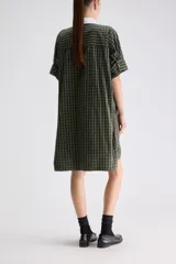 Vestido camisero midi de calce relajado a cuadros en tonos verde y negro, confeccionado en algodón liviano. Presenta cuello clásico en contraste de color blanco, cartera frontal oculta con botones y mangas cortas con vuelta.