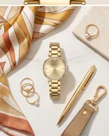 Reloj de pulsera analógico para mujer, con caja redonda de metal dorado y bisel decorado con cristales. Presenta una esfera minimalista en tono dorado con manecillas finas y una malla de eslabones metálicos a juego.