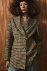 Blazer de corte entallado con estampado de cuadros, cuello solapa y cierre frontal cruzado con botones. Presenta mangas largas con detalle de abertura y botones en los puños, y forro interior a contraste.