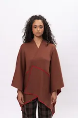 Ruana de algodón en color marrón con detalles de costura a mano en contraste color rojo en los bordes. Diseño envolvente de corte asimétrico y mangas amplias.