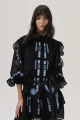 Blusa negra de viscosa con bordados florales azules en el frente y las mangas, cuello mao y mangas 3/4 abullonadas con volados. Incluye cinturón fino con hebilla metálica.