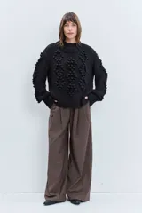 Sweater de punto grueso color negro, con diseño de textura en relieve tipo pompones y cuello redondo. Presenta un corte holgado y mangas largas.