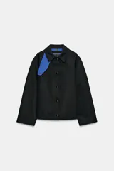 Chaqueta de Zara Woman Collection color negro, de cuello con solapa y manga larga. Cuenta con bolsillos delanteros ocultos en las costuras, cierre frontal con botones metálicos a presión y detalle de diseño asimétrico en azul en el cuello.