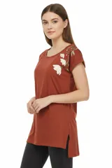 Remera color terracota de manga corta, con cuello redondo y diseño holgado, con estampa de flores blancas y hojas verdes en la zona del hombro y pecho.