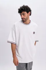 Remera manga corta blanca de corte holgado, con cuello redondo y puños acanalados en tono bordó con líneas blancas. Cuenta con un pequeño bordado circular en el pecho con la inscripción "NYC Well-Being Association" y un diseño de red.
