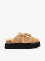 Zueco color beige con plataforma negra, capellada de cuero y plantilla recubierta en piel de oveja. Presenta una hebilla metálica de gran tamaño en la capellada.