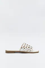 Sandalia baja blanca con capellada entrelazada y apliques de tachas metálicas plateadas.