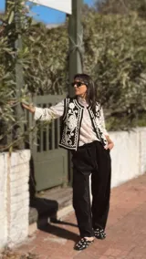 Chaleco negro con bordados blancos de estilo arabesco en el frente, sin mangas y con diseño abierto.