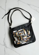 Bandolera de cuero negro Carolina De Cunto, con detalle de arte abstracto pintado a mano en tonos dorados, plateados y blancos. Cuenta con correa ajustable, herrajes metálicos y cierre superior.