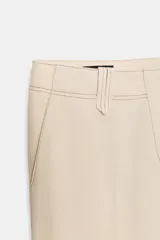Pantalón de tiro alto con trabillas, bolsillos laterales y cierre frontal con cremallera y gancho metálico. Presenta un diseño de corte recto con costuras decorativas a contraste en la cintura y el ruedo.