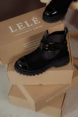 Bota corta de cuero negro con suela track, puntera de charol y estribo desmontable con hebilla metálica.