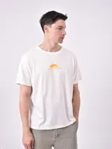 Remera de manga corta color beige, con cuello redondo y un pequeño estampado frontal que simula un atardecer o amanecer en el desierto con el texto "SOUL OF THE DESERT".