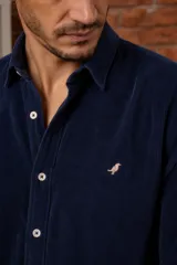 Camisa azul marino de pana, de corte slim fit, con cuello clásico, botones delanteros claros y detalle de ave bordada en el pecho.