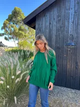 Buzo verde de lana y poliamida, con diseño oversize, cuello redondo y trenzas en la parte delantera.