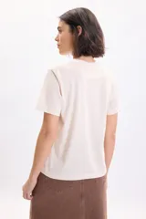 Camiseta de manga corta color crudo con cuello redondo y estampa frontal en tono bordó con motivos florales y texto tipográfico.