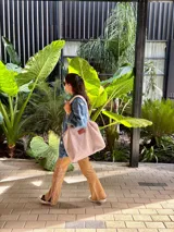 Bolso tipo tote confeccionado en corderito sintético color beige, con cierre principal y bolsillo interior. Presenta una etiqueta de cuero sintético en el frente.