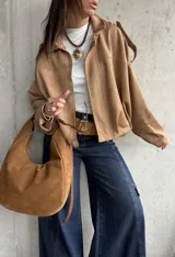 Campera tipo bomber de gamuza con diseño relajado, cierre frontal, cuello camisero y detalles de apliques en los hombros.