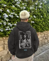 Canguro con capucha de algodón y poliéster, color negro con efecto acid wash, corte regular fit y estampa en la espalda con diseño en blanco y negro de una persona con un gato dentro de un sello postal, acompañada de texto en celeste.