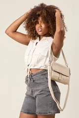 Bandolera de ecocuero color beige con tapa frontal, cierre superior y correa regulable.