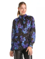Blusa de gasa plisada con estampado floral en tonos azules y violetas sobre fondo negro. Presenta cuello alto, mangas largas con puños abotonados y un diseño fluido con textura plisada.