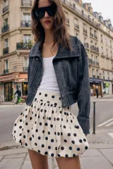 Falda pantalón de estilo globo con diseño abullonado y estampado de lunares negros sobre fondo crudo. Presenta cintura alta y cierre lateral con cremallera oculta.