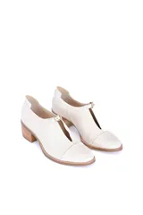 Zapato cerrado tipo mocasín con taco cuadrado de madera, confeccionado en cuero con textura de reptil en color crema. Presenta un detalle de hebilla metálica dorada en el empeine.