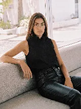 Blusa sin mangas de lino color negro, con silueta recta y relajada, cuello alto plisado y cartera lateral asimétrica con pliegues y botones forrados al tono.
