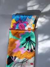 Pañuelo cuadrado de seda con estampado floral multicolor que combina tonos rojos, amarillos, azules y fucsias sobre fondo blanco, con borde rojo.