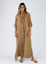 Vestido largo de lino color tostado, con diseño camisero, botonadura frontal completa con detalles de volados a lo largo de la botonadura, mangas largas arremangables y aberturas laterales en el bajo.