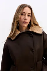 Campera de estilo aviador en color marrón oscuro, con exterior efecto gamuza e interior de corderito sintético color beige. Presenta cuello amplio, cierre frontal con botones y bolsillos laterales.