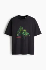Remera oversized negra de punto de algodón pesado, con cuello redondo acanalado, hombros caídos, mangas cortas y estampa frontal de la banda Gorillaz en un vehículo militar con detalles en verde.