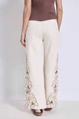 Pantalón de jean color crudo con bordados florales y aberturas en las piernas.