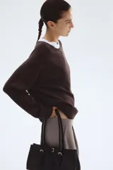 Buzo de punto fino color marrón oscuro, de corte holgado con escote redondo y mangas raglán. Presenta puños y bajo acanalados.