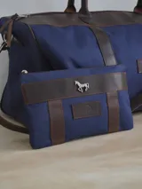 Sobre o cartuchera de lona fucsia con terminaciones y detalles de cuero marrón. Cuenta con cierre superior y aplique metálico de caballo en la parte frontal, además de una etiqueta de cuero con la marca grabada.
