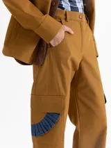 Pantalón de gabardina color marrón, de tiro alto y silueta estructurada. Cuenta con volados de denim azul aplicados sobre los bolsillos plaqué laterales y bolsillos plaqué traseros con remache dorado.