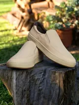 Zapatillas tipo slip-on color beige, con textura microperforada en la parte superior, suela de goma al tono y detalle de refuerzo en el talón en color marrón oscuro.