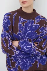 Buzo de tejido de punto con diseño floral en contraste, cuello redondo y mangas largas. Presenta una textura suave y un corte holgado.