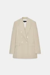 Blazer de mujer color beige claro, de corte largo y cruzado con doble botonadura. Presenta cuello solapa y bolsillos delanteros de ojal.