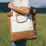 Bolso tote de color marrón con bolsillo frontal blanco y asas de hombro en tono crudo.