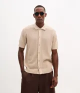Camisa de punto color beige con textura, de manga corta, cuello inglés y cierre frontal de botones.